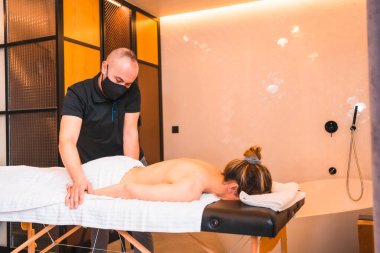 Evde masaj yapmak, müşterinin evinde kollarında masaj yapmak. Koronavirüs salgınında bir maskeyle