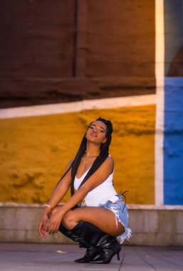 Şehirdeki bir sokakta örgü ören Afrikalı bir kızla şık bir şehir tarzı. Beyaz gömlek ve pantolon, dikey fotoğraf.