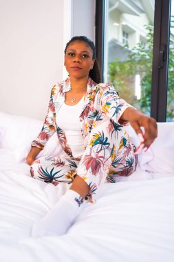 Bir otel yatağında pijamalarıyla yatağın üstünde yaşam tarzı. Siyahi etnik kız ve gülümseme