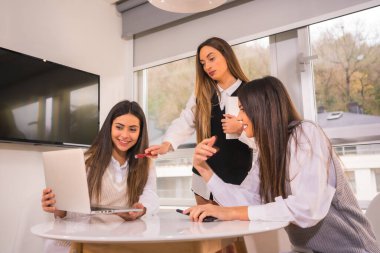 Beyaz tişörtlü bilgisayarla gayri resmi toplantıdaki genç iş kızları. Evdeki bir masada gayri resmi toplantı.