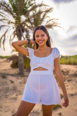 Beyaz elbiseli, palmiye ağacının yanında plaj tatili yapan esmer bir kadının yaşam tarzı.