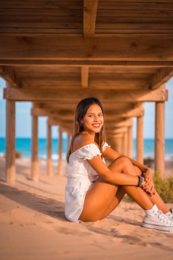 Beyaz elbiseli, kumsalda tatilin tadını çıkaran esmer bir kadının yaşam tarzı.