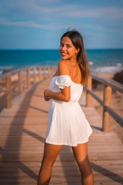 Kumsalda tatilde olan beyaz elbiseli, genç esmer bir beyazın yaşam tarzı. Tahta kaldırım boyunca yürüyor.