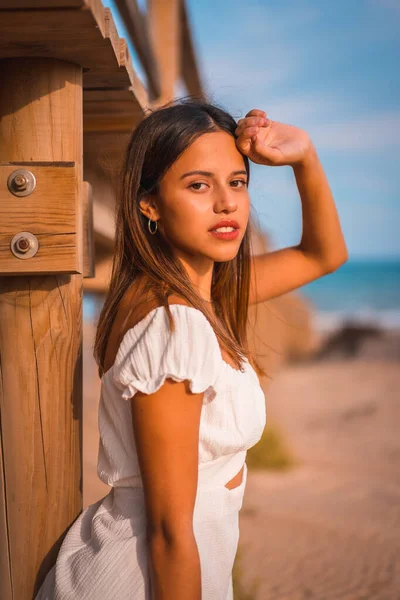 Beyaz bir elbiseyle yaz tatilinin tadını çıkaran beyaz tenli bir esmerin yaşam tarzı, ahşap bir geçidin yanında.