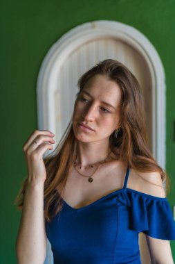 Yazın mavi elbiseli, genç, kızıl saçlı beyaz bir kızın yaşam tarzı yeşil bir evin beyaz kapısının yanında dikey bir fotoğraf çekilmişti.