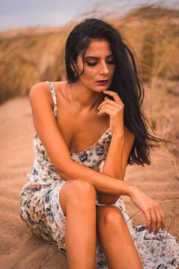 Beyaz çiçekli bir elbiseyle saçlarını okşayan esmer bir beyazın portresi, Nijar 'daki Cabo de Gata sahilinde kumsalda oturuyor. Endülüs, İspanya