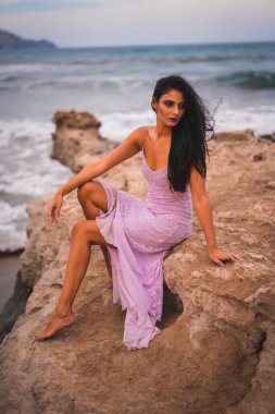 Kumsalda deniz kenarında eğlenen pembe elbiseli esmer bir beyaz kadın pozu.