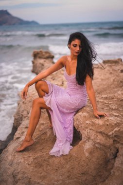Kumsalda deniz kenarında eğlenen pembe elbiseli esmer bir beyaz kadın pozu.