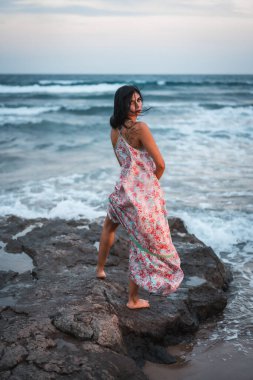 Kumsalda deniz kenarında tatilin tadını çıkaran, beyaz kumaşlı, çiçekli beyaz bir beyaz kadın pozu.