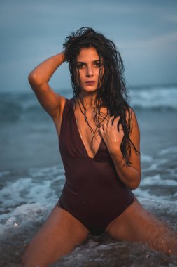 Kumsalda tatilin tadını çıkaran bordo mayo giymiş beyaz bir esmerin şehvetli bakışları.