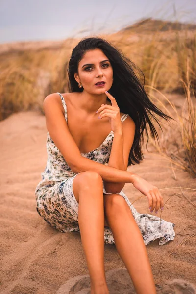 Morena Caucásica Acariciando Cabello Con Vestido Floral Blanco Sentada Arena — Foto de Stock