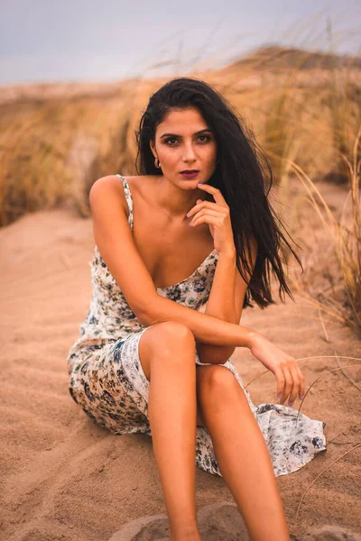 Beyaz çiçekli bir elbiseyle saçlarını okşayan esmer bir beyazın portresi, Nijar 'daki Cabo de Gata sahilinde kumsalda oturuyor. Endülüs, İspanya