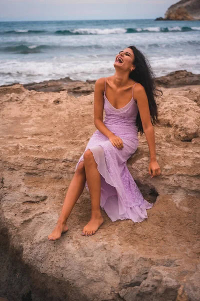 A brunette Caucasian in a pink dress, on the beach having fun by the sea