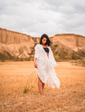 Beyaz elbiseli ve siyah bikinili esmer bir mankenin portresi. Bir yaz günü, güzel bir çölde.