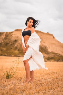 Beyaz bir elbise ve siyah bir bikini giyen esmer bir mankenin portresi güzel bir çölde, bir yaz öğleden sonra, dikey bir fotoğraf.