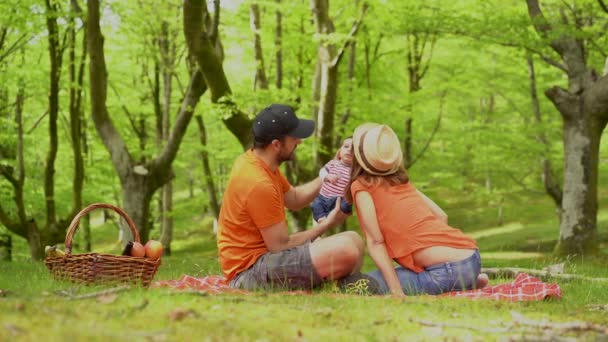 一家人在野餐日和他们刚出生的儿子在一起穿着橙色T恤衫和帽子 享受暑假生活 — 图库视频影像