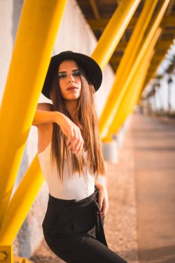 Siyah şapkalı ve pantolonlu, sarı tahta kaldırımda genç bir esmer.