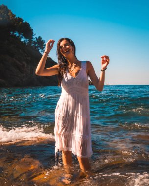 Beyaz elbisesiyle deniz suyunda banyo yapan beyaz tenli genç bir esmer. Yaz yaşam tarzı.