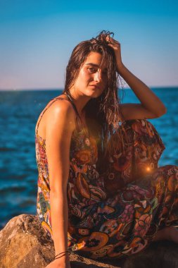 Arkadan sırılsıklam sırıtan beyaz bir kadının portresi ve deniz kenarında çiçekli bir elbise.