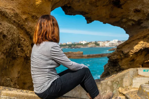A young woman looking in a window on the rocks next to Plage du Port Vieux in Biarritz, on vacation in southeastern France. Biarritz, department of Pyrenees-Atlantiques