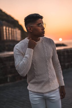 Yaz yaşam tarzı, yaz tatillerinin tadını çıkaran genç bir Latin. Beyazlar içinde, pantolon ve süveter içinde, deniz kenarında yürüyor.