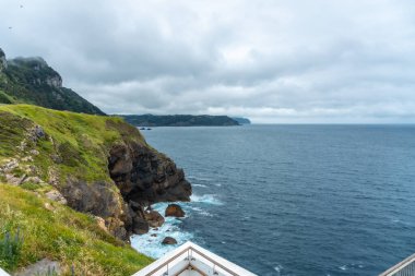 Bulutlu bir bahar sabahı, Santa Catalina de Lekeitio deniz fenerinin yanındaki kayalıklarda, arka planda deniz, Bizkaia manzaraları. Bask Ülkesi