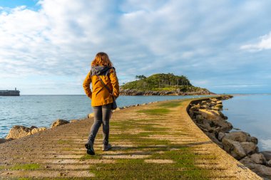 A young tourist on the footbridge to go to San Nicolas Island at low tide from Isuntza beach in Lekeitio, Basque Country. Bay of Biscay. Spain clipart