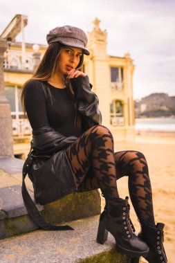 Yaşam tarzı, yaz tatilinde kumsalın yanında kısa siyah bir elbise ve ekose çoraplı esmer bir beyaz kadın pozu.