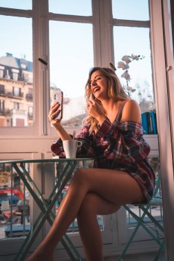 Genç bir sarışının kahvaltı edişinin yaşam tarzı evinin yanında kahvaltı etmesidir. İç çamaşırı ve pijama giymiş, sosyal medyaya gülümsüyor.