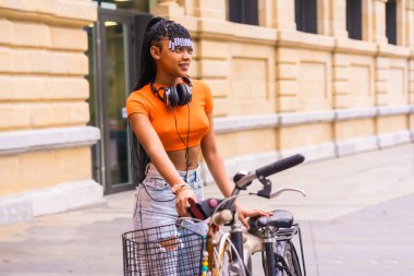 Şehirde genç bir kapan dansçısıyla yaşam tarzı. Turuncu tişörtlü ve kovboy pantolonlu Afrikalı etnik grubun siyah kızı. Şehirde park etmiş bisikleti boyuyorum.