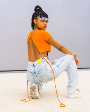 Örgülü genç bir tuzak dansçısı. Turuncu tişörtlü ve kovboy pantolonlu zenci etnik kız. Back Agachada 'nın arkası baştan çıkarıcı görünüyor.