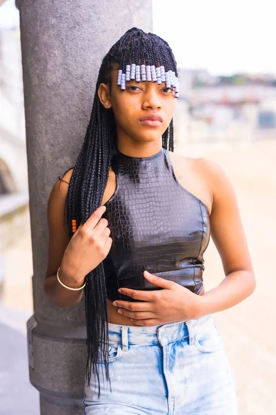 Black ethnic girl with braids with leather top and cowboy pants. Enjoying summer holidays next to the beach, vertical photo