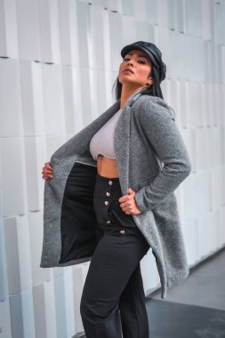 Deri şapkalı, gri ceketli, gri şehir arkaplanlı, esmer bir Latin.