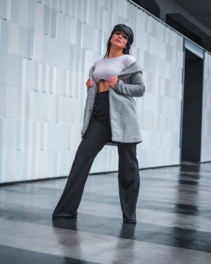 Deri şapkası ve gri yağmurluğu olan güzel Latin bir kızın şehrinde sokak tarzı.