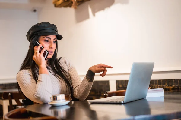 拉丁黑发设计师用咖啡店的笔记本电脑打了一个工作电话 — 图库照片