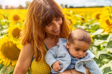 Beyaz bir anne ve bebeğinin portresi Ayçiçeği tarlasında eğleniyor, yaz yaşam tarzı