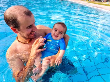 İlk kez havuzda bebeğini yıkayan beyaz bir baba.