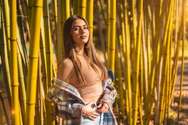 Bambu ormanlarında sonbahar yaşam tarzı, ekose yün kazaklı genç esmer kız, sola bakıyor.