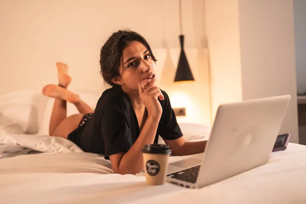 在床上放轻松性感的黑发女孩 带着电脑和咖啡 阅读社交网络 — 图库照片