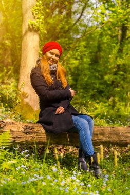 Siyah ceketli ve kırmızı şapkalı bir kadın sonbahar parkında gün batımında gülümsüyor.