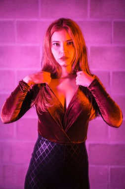 Lateks giymiş seksi kızıl kız, tuğla bir duvarda kahverengi ve siyah bir vücut giysisi, geceleri pembe ışıkla aydınlatılmış.