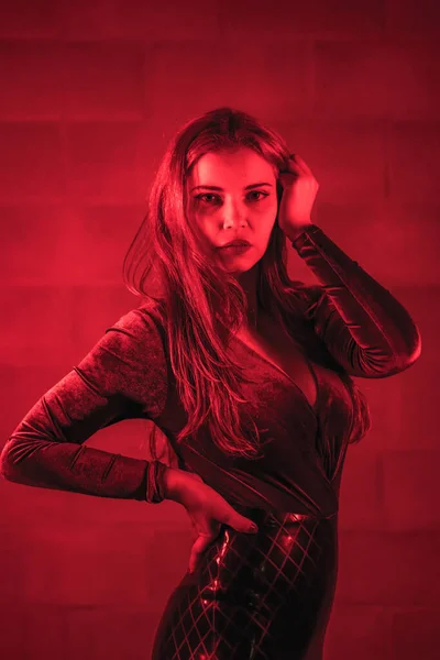 红头发姑娘 身穿乳胶 棕色和黑色紧身衣 挂在砖墙上 夜晚点着红光 — 图库照片
