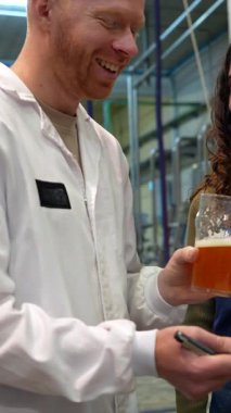 Neşeli bira ustası ve bayan meslektaşı modern bir bira fabrikasında yeni bir zanaat birasını tadıp analiz ederken, zanaat ürünlerinin en yüksek kalitesini sağlamak için özelliklerine dikkat çekiyorlar.