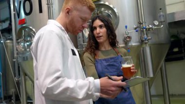 Profesyonel bayan biracı ve erkek meslektaşı yeni demlenmiş bir biranın kalitesini inceliyor. Bira fabrikasında büyük çelik fermantasyon tanklarının yanında dururken karakteristik özelliklerini tartışıyor.