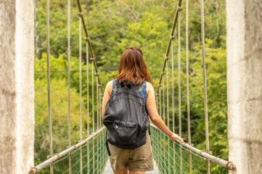 Sırt çantalı kadın turist, asturya, İspanya 'da yemyeşil ormanlarla çevrili Sella nehri üzerindeki asılı bir köprüde yürüyor ve yaz macerasının tadını çıkarıyor.