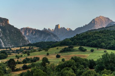 Golden hour sunlight illuminating the iconic naranjo de bulnes peak, towering over lush green valleys and forests in picos de europa national park, asturias, spain