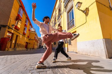 İki enerjik genç adam bir kaldırım taşı caddesinde dinamik bir dans gösterisi sergiliyor. Parlak güneş ışığı renkli şehir mimarisini aydınlatırken mutluluk ve özgürlüğü ifade ediyorlar.
