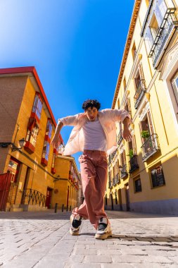 Tarz sahibi genç bir adam dinamik bir sokak dansı yapıyor. Avrupai bir şehir bölgesindeki kaldırım taşları üzerinde hareket ediyor. Uzun boylu, güneşli, enerjik bir yaz sahnesi.