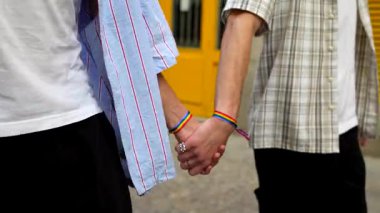 Igbt gökkuşağı bilezikleriyle genç bir çift şehir caddesinde el ele yürürken, şefkatli ve destekleyici bir şekilde sevgilerini gösteriyorlar.