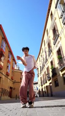 Genç erkek dansçı, tarihi bir Avrupa şehrinin kaldırım taşı caddesinde anlamlı bir modern dans gösterisi sergiliyor. Güneşli bir günde akışkan hareketlerini ve sanatsal tutkusunu sergiliyor.